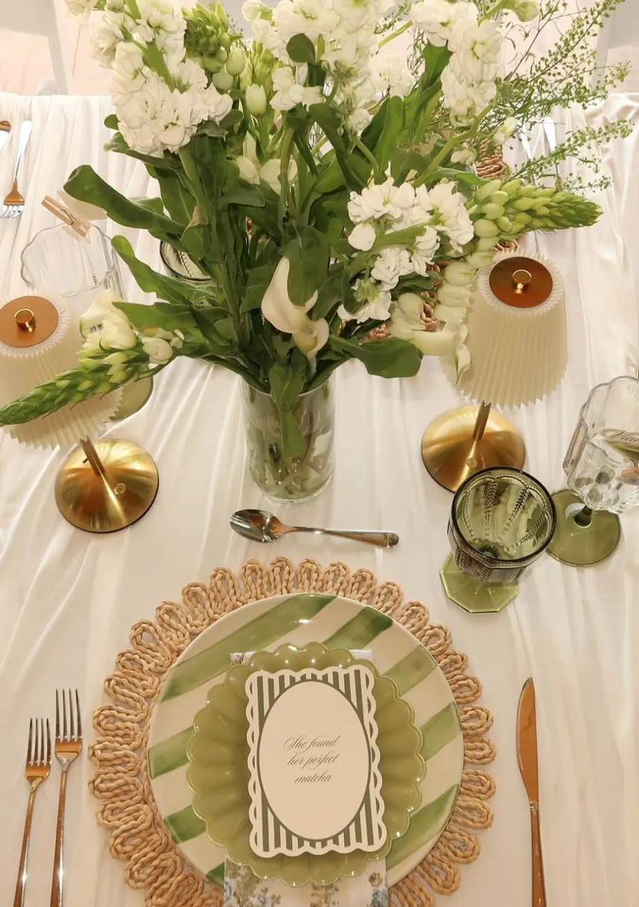 Styled tablescape with white florals, gold lamps and a rattan charger