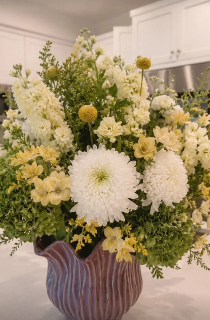 White chrysanthemum and yellow floral arrangement in a ruffled vase